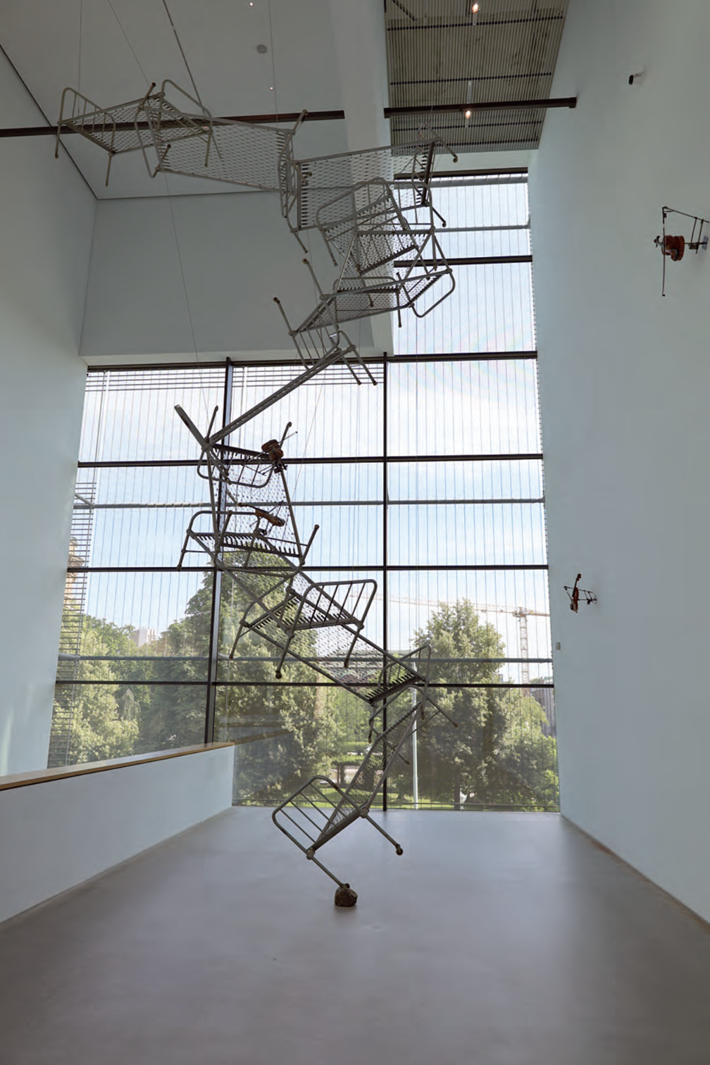 Kunstinstallation aus übereinander gestapelten Metallbetten in heller Galerie vor großem Fenster